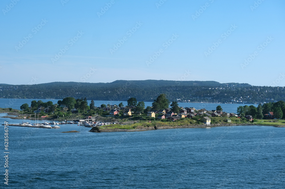 Norwegen im Sommer: Impression eines kleines Hafens und landestypischer Gebäude und Ferienhäuser auf einer Insel im Oslofjord, in der Nähe der norwegischen Hauptstadt Oslo, blauer Himmel