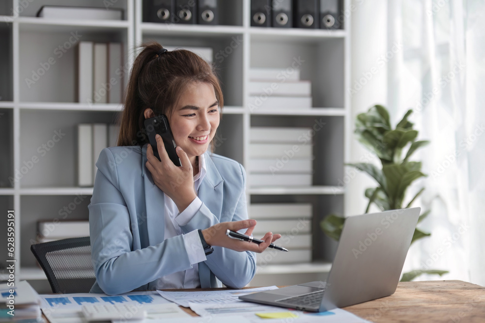 Portrait of young business woman with sitting in office in front of her laptop and talking on mobile phone hand at office Portrait of young business woman with sitting in office in front of her laptop and talking on mobile phone hand at office