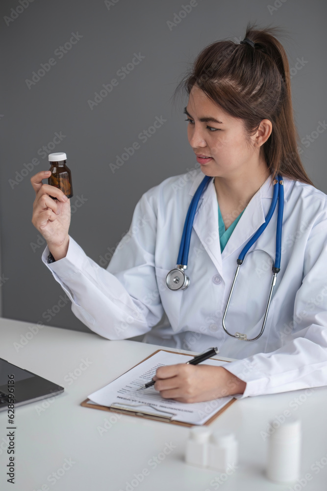 Young beautiful asian woman doctor holding pills bottle writing on document at clinic Young beautiful asian woman doctor holding pills bottle writing on document at clinic