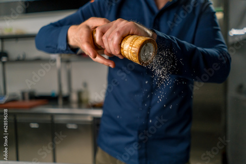 close-up of a chef holding a pepper and salt grinder in his hands grains of spices fall in the air