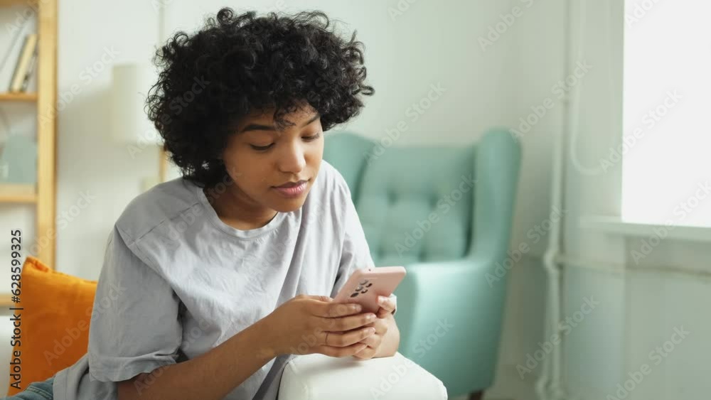 African girl holding smartphone touch screen typing scroll page at home. Woman with cell phone surfing internet using social media apps playing game. Shopping online Internet news cellphone addiction