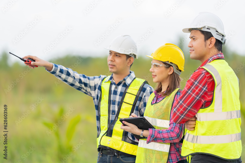 Group photo of a team of 3 Asian male and female engineers with a technician manager wearing a vest, walkie-talkie and helmet working together using a tablet. point to destination Plan future industry Group photo of a team of 3 Asian male and female engineers with a technician manager wearing a vest, walkie-talkie and helmet working together using a tablet. point to destination Plan future industry