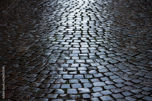 Cobblestone in a narrow street in Stresa, Italy. Wet shiny historic basalt ashlars or blocks reflecting blue sky and sunshine after rain. Old pavement background with typical surface and structure. photo