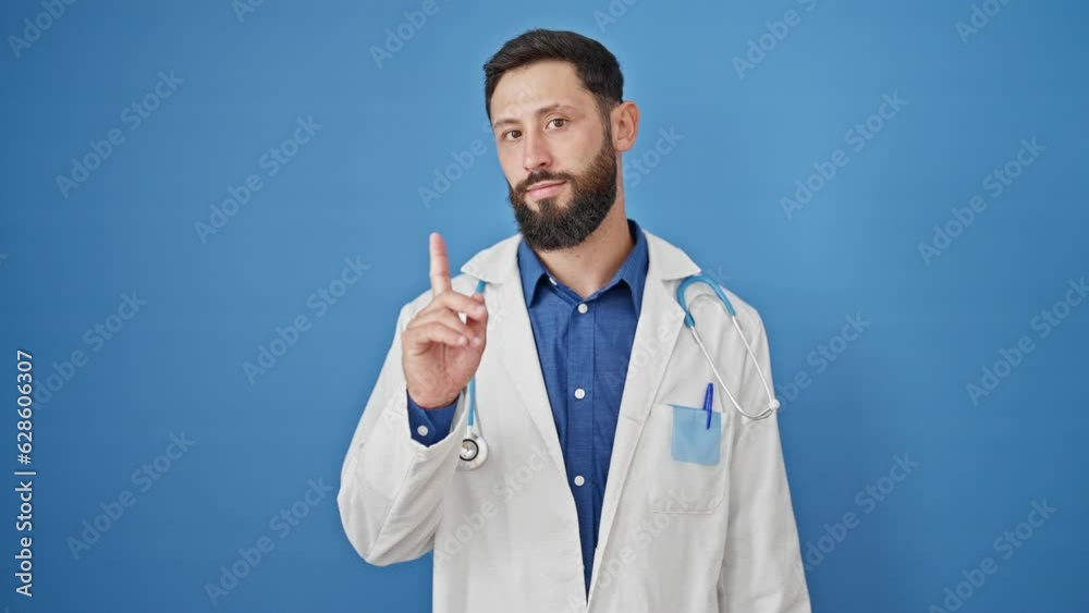 Young hispanic man doctor standing with serious expression saying no with finger over isolated blue background Young hispanic man doctor standing with serious expression saying no with finger over isolated blue background