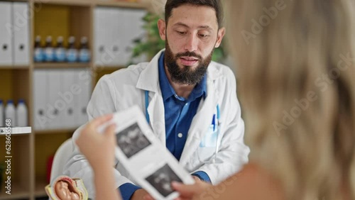 Young hispanic man gynecologist showing ultrasound to patient at the clinic photo