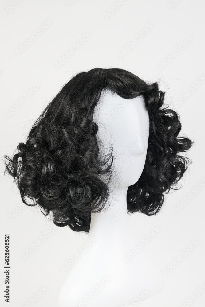Fototapeta premium Natural looking black wig on white mannequin head. Medium length curly wavy hair on the metal wig holder isolated on white background, side view