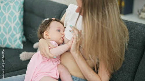 Mother and daughter sitting on sofa breastfeeding baby at home