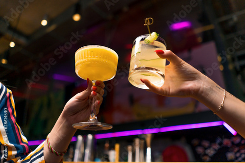 Close up of two people cheering cocktails in bar or a disco club drinks and cocktails concept