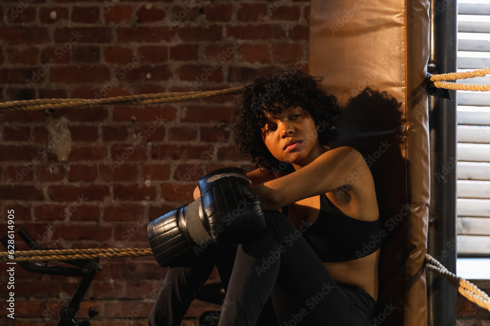 Woman fighter girl power. African american woman fighter with boxing gloves sitting on boxing ring waiting and resting after fight. Strong powerful girl in gym. Strength fit body workout training Woman fighter girl power. African american woman fighter with boxing gloves sitting on boxing ring waiting and resting after fight. Strong powerful girl in gym. Strength fit body workout training