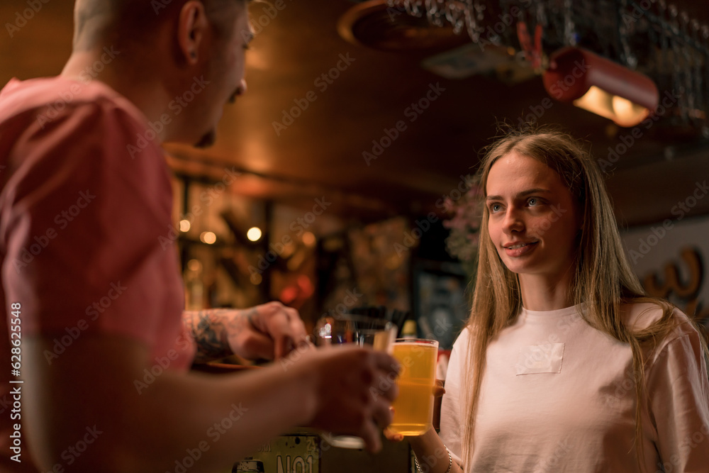 A young smiling girl with a glass of beer in her hand is chatting with a man at the bar in a club bar 