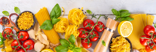 Various pasta with spices and ingredients for cooking. Preparation dinner, lunch background with fresh basil, tomatoes, spices, garlic and different sort and types of italian Mediterranean pasta