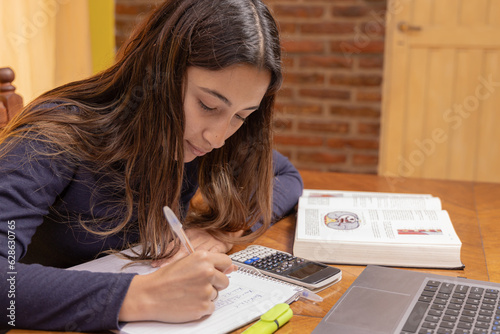 Latin girl studying on a table with school supplies.