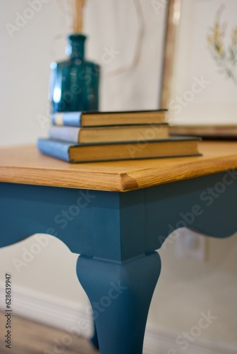 Blue chalk painted end table with wood top decorated with books, vase and illustration.