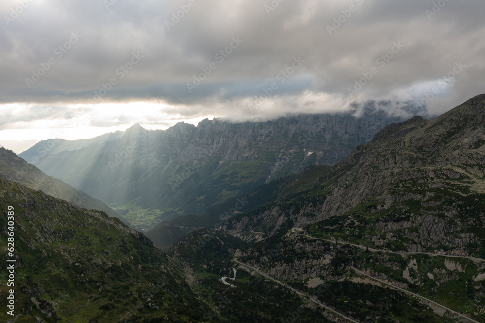 Drone view of majestic Swiss alps with green grass under cloudy sunset sky during sundown time in Switzerland.