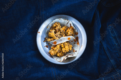 Breakfast chorizo and eggs tacos on a plate against a blue denim jacket