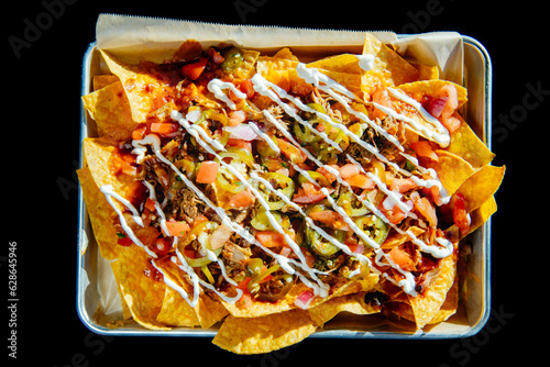 Pulled pork nachos on a tray with parchment paper against a black background, with sour cream drizzled on top