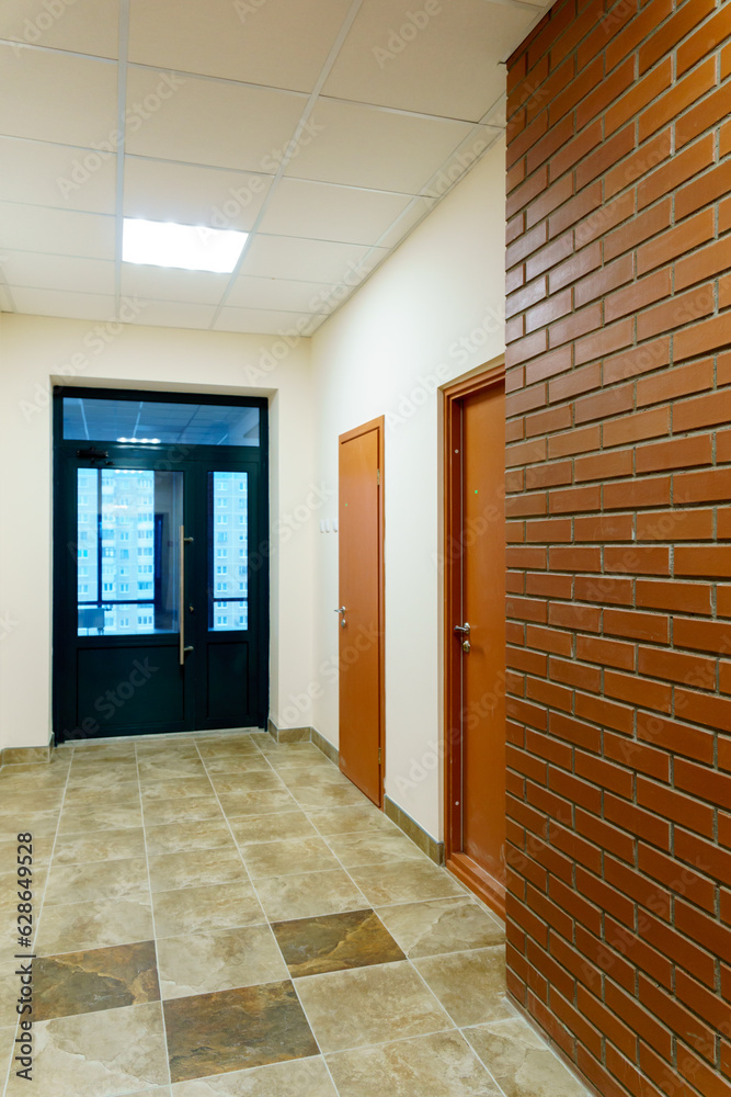 Obraz premium Decorative brick on the corridor wall in an office building. A black glass door at the end of the corridor of the business center. Interior design in the Art Nouveau style.
