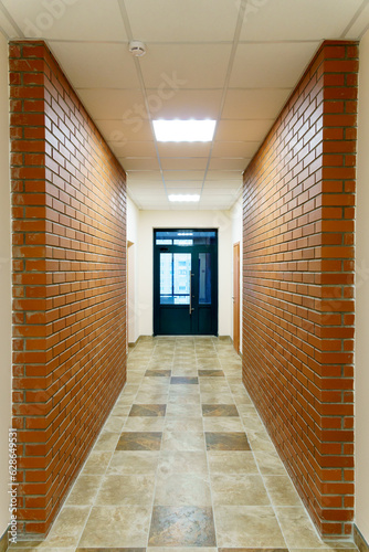 Decorative brick on the corridor wall in an office building. A black glass door at the end of the corridor of the business center. Interior design in the Art Nouveau style.