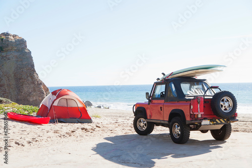 Red Jeep with surfboard at the beach next to camp tent