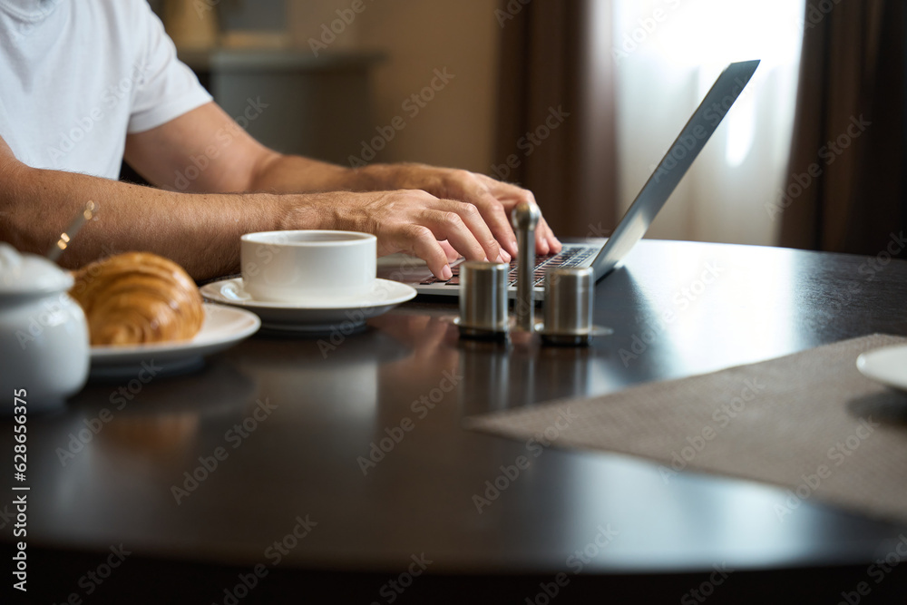 Middle-aged male sits at a table with a laptop and a light breakfast Middle-aged male sits at a table with a laptop and a light breakfast