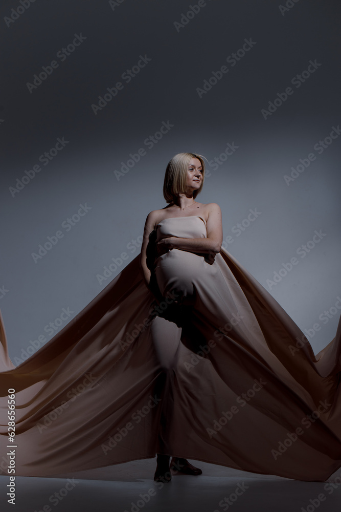 A pregnant woman with white hair of Caucasian appearance is wearing a beige sheet that flies beautifully on the background. A pregnant woman with white hair of Caucasian appearance is wearing a beige sheet that flies beautifully on the background.