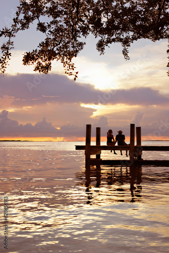 couple sitting on dock silhouette at sunset at ocean