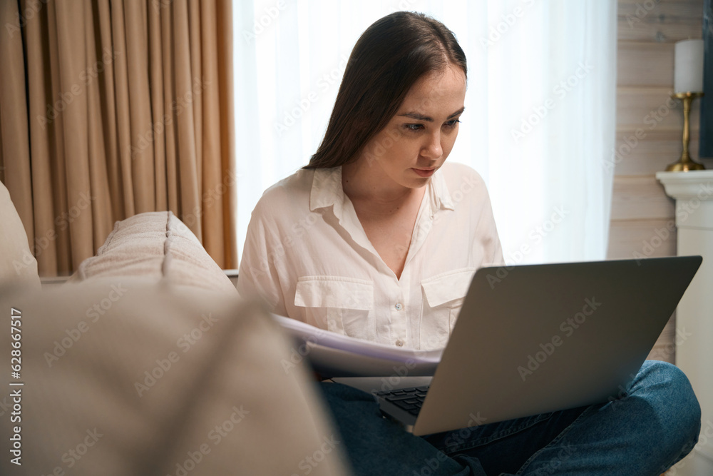 Pretty young lady freelancing while checking documents