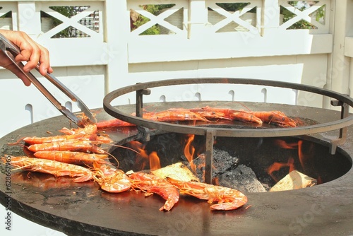 Seafood slices are cooked on a fire pit surface in the shape of cone shaped bowl. Bowl-shaped flat grill with prawns and shrimps. Outdoor barbecue cooking. Street food concept. Toast the hot grilled photo