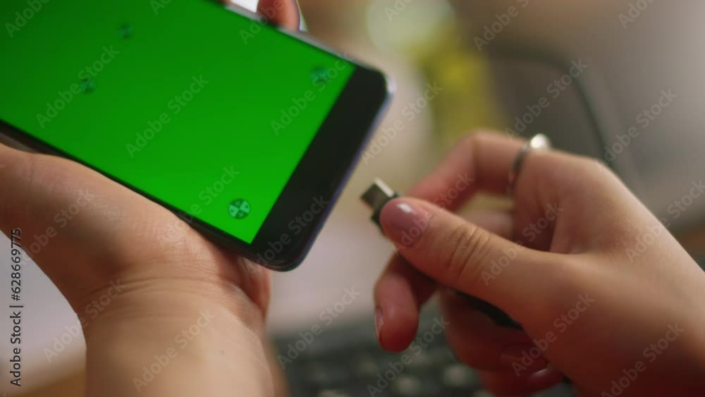 closeup of hands with painted nails connecting cable to smartphone