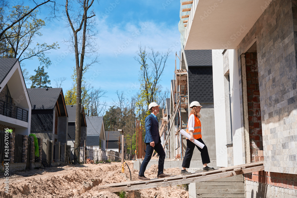 Forewoman in safety vest going with inspector to house under construction Forewoman in safety vest going with inspector to house under construction