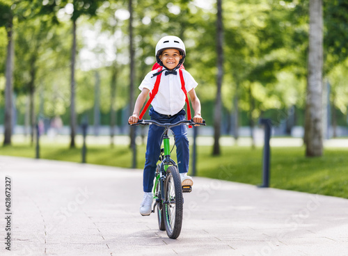 Fototapeta Naklejka Na Ścianę i Meble -  Happy ethnic child schoolboy in a helmet and with a briefcase rides a bike to school.