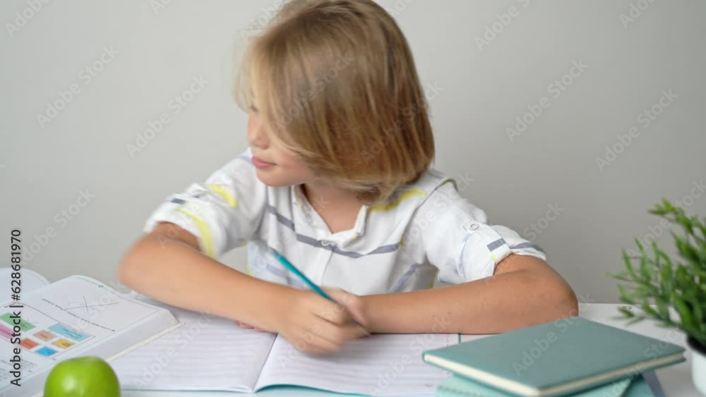 Middle school smiling student boy sitting at desk, studying writing book homework and tablet at class home Back to school. Childhood, education for children