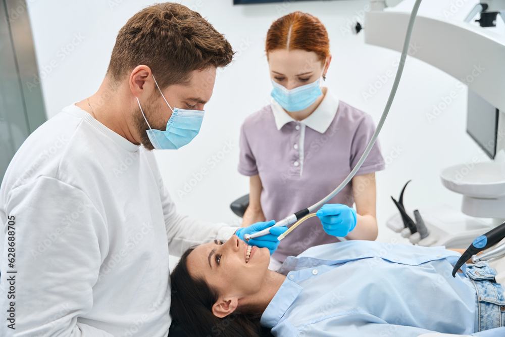 Professional dentist in uniform talking to female client during teeth treatment Professional dentist in uniform talking to female client during teeth treatment