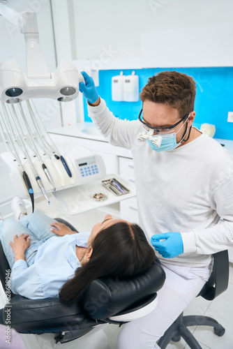 Qualified dental technician in dental magnifying glasses preparing workplace