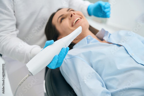 Stomatologist in uniform taking intraoral camera to examine mouth inside