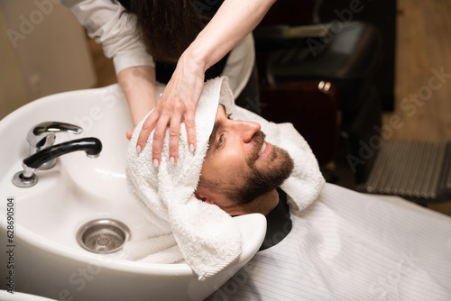 Female barber dries head of a man with soft towel