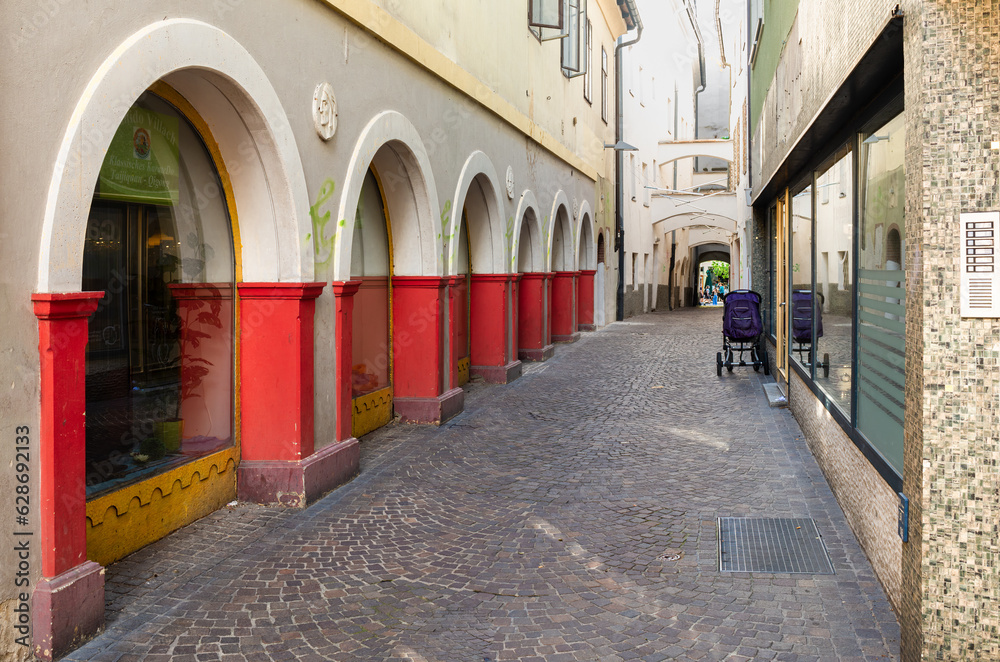 Fototapeta premium Villach, Austria - July 12, 2023: A street with arcades, partly red, in the old town of Villach