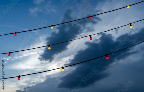 Red and yellow electric lights on cables and a dramatic sky with dark clouds in the background