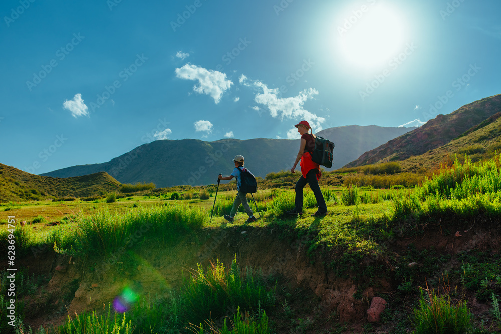 Young woman hiker and her son walking through a mountain valley with backpacks at sunset