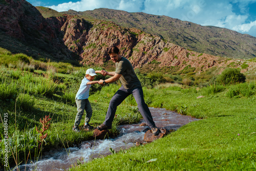 Father helps his son cross mountains stream photo