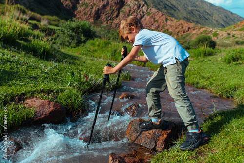 Boy with trekking poles checks the depth of mountain stream photo