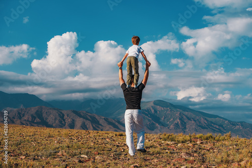 Boy standing on his father's shoulders on mountains background