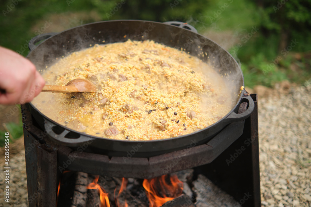 Cooking porridge with meat in a cauldron on an open fire, in nature Cooking porridge with meat in a cauldron on an open fire, in nature