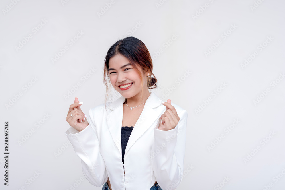A playful and happy young woman using her thumb and forefinger to create a finger heart gesture with both hands. Isolated on a white background. A playful and happy young woman using her thumb and forefinger to create a finger heart gesture with both hands. Isolated on a white background.