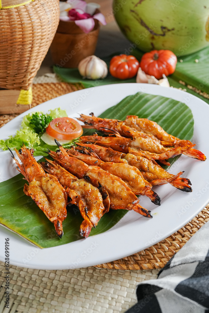 Grilled prawns with honey served on the banana leaf with some garnish. Indonesian food photography. Indonesian seafood. Dark mood food photography. 