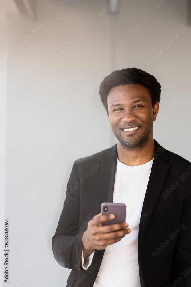Handsome african american man holding mobile phone checking email standing in modern office