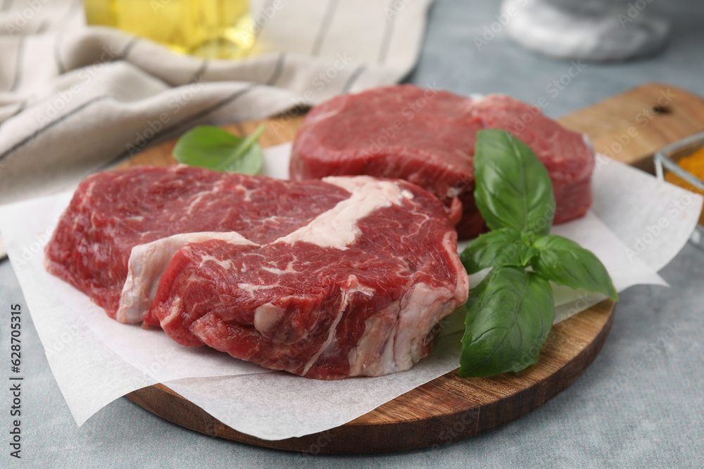 Fresh raw cut beef and basil leaves on grey table, closeup