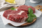 Fresh raw cut beef and basil leaves on grey table, closeup