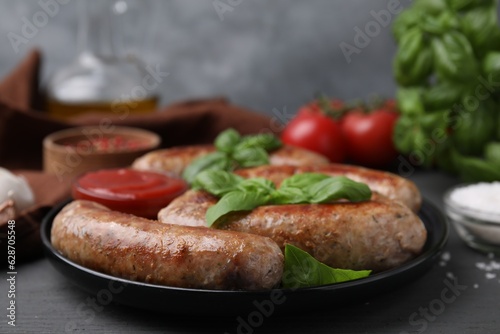 Tasty homemade sausages and basil leaves on grey wooden table, closeup