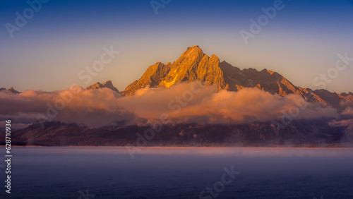 Clouds hanging over Jackson Lake as the sun rises and lights up the tallest peaks of Grand Teton National Park, Wyoming, USA © hpbfotos
